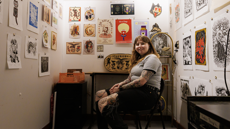 An art student sits surrounded by her artwork.