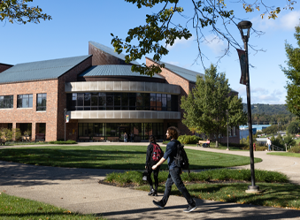 Students walking along a sidewalk with a campus library in the background.