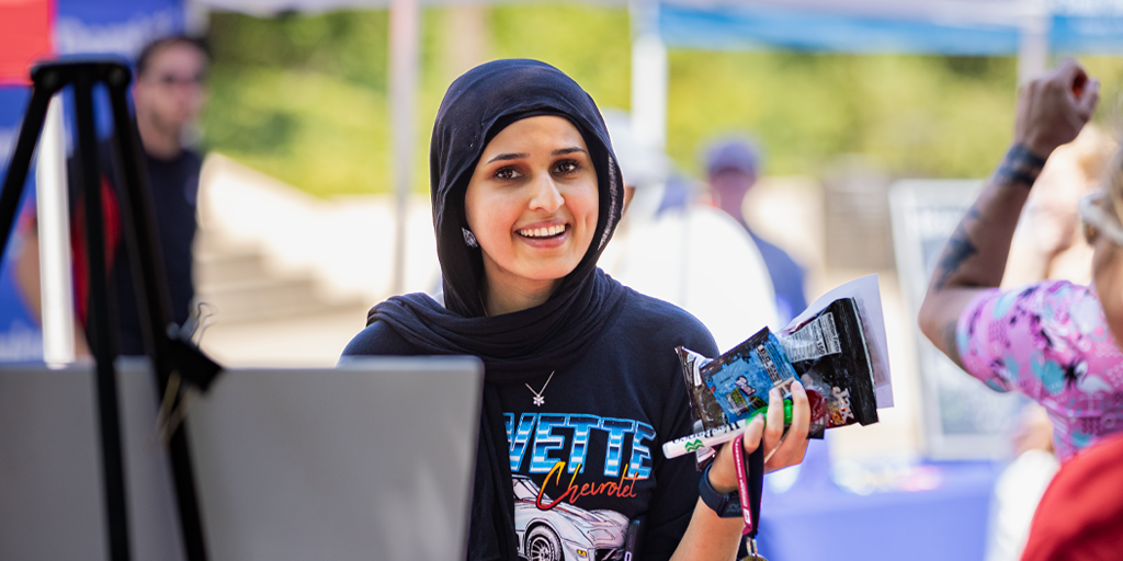 A female student smiles at the camera during an outdoor campus event.