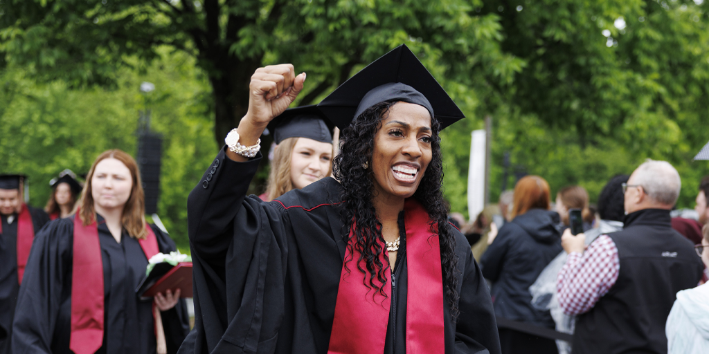An African-American female college graduate smiles in a crowd of other college graduates.