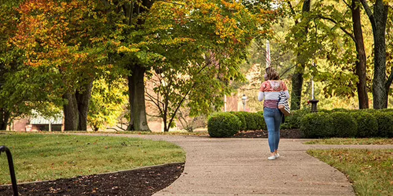 A student walking on IU Southeast's campus surrounded by fall foliage.