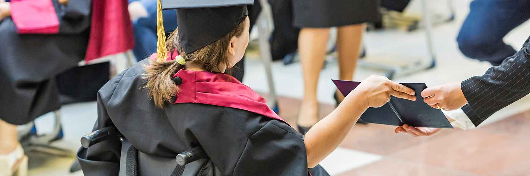 Female student in a wheelchair receiving a diploma.