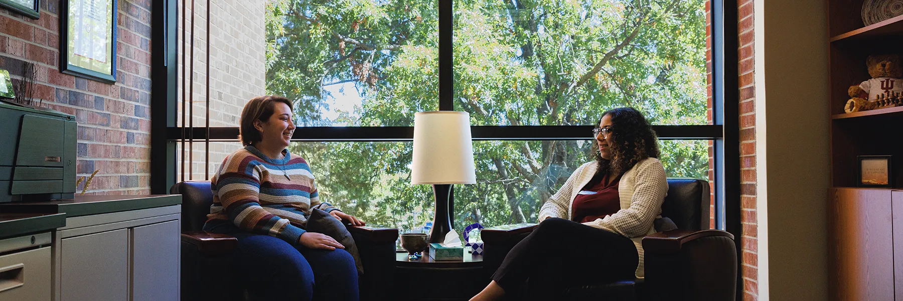 A student and counselor sitting in chairs across from each other in an office and smiling