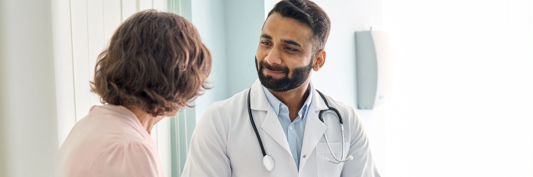 Physician wearing white coat talking to woman signing medical paper at appointment visit in clinic.
