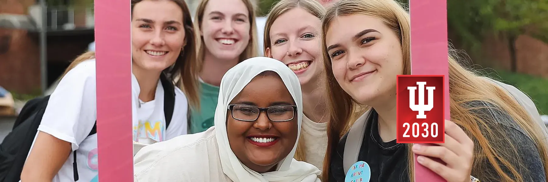 Five students smiling behind a photo frame prop