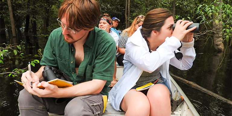 Students exploring in a boat taking notes and looking through binoculars