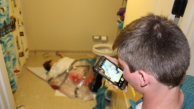 A forensic psychology student takes a photo of a "dead" student at a crime scene reconstruction.