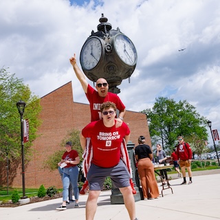An IU day parade goer is held on the back of an IU student, both dressed in IU t-shirts.