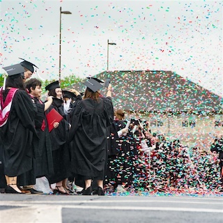 2024 IU Southeast graduates in academic regalia celebrate with confetti poppers.