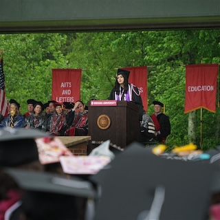 Student Speaker Keziah Jones dressed in academic regalia speaks before a crowd of graduates.