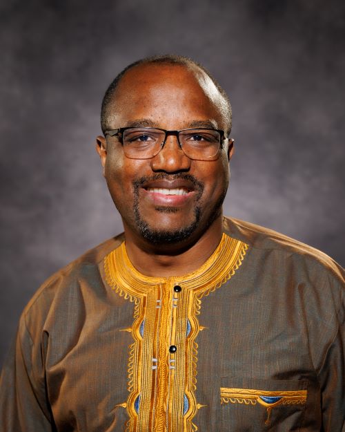 Dr. Victor Waingeh in a brown and yellow shirt in front of a grey backdrop